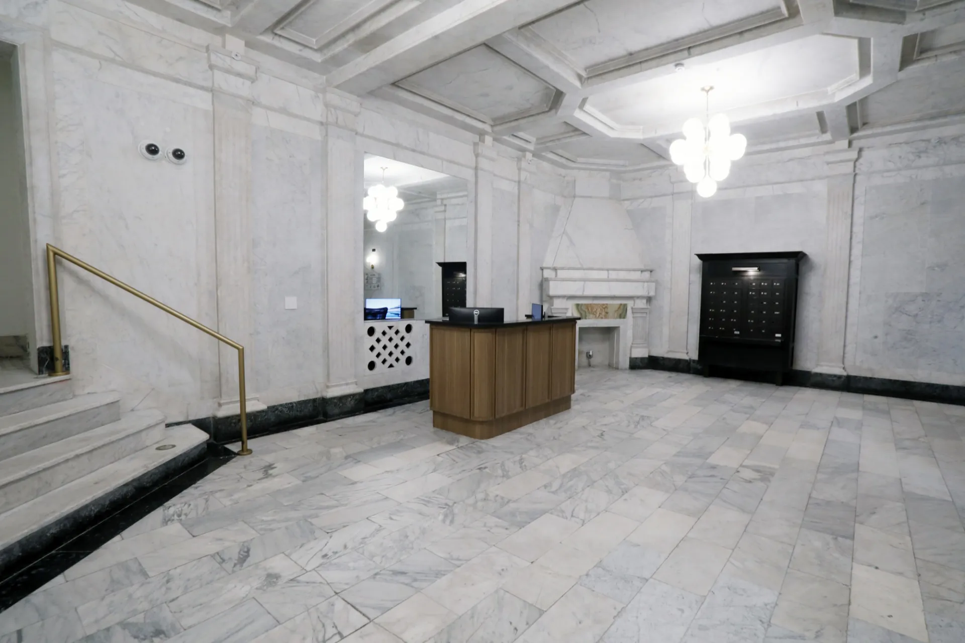 A white marble lobby with a wood accent receptionist desk and black mailbox.