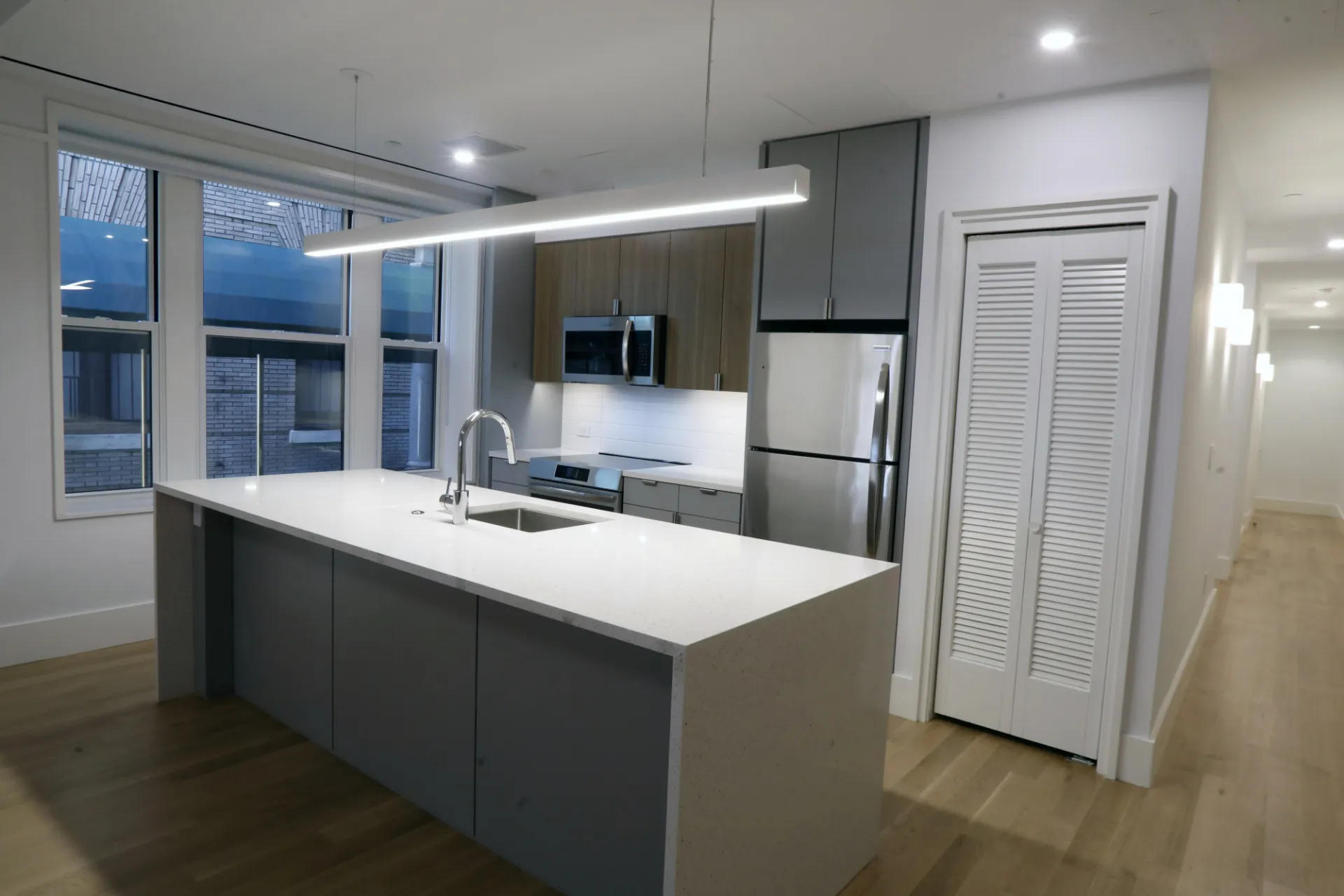 A renovated apartment with a white kitchen island with gray accents, and wood and gray cabinetry. 
