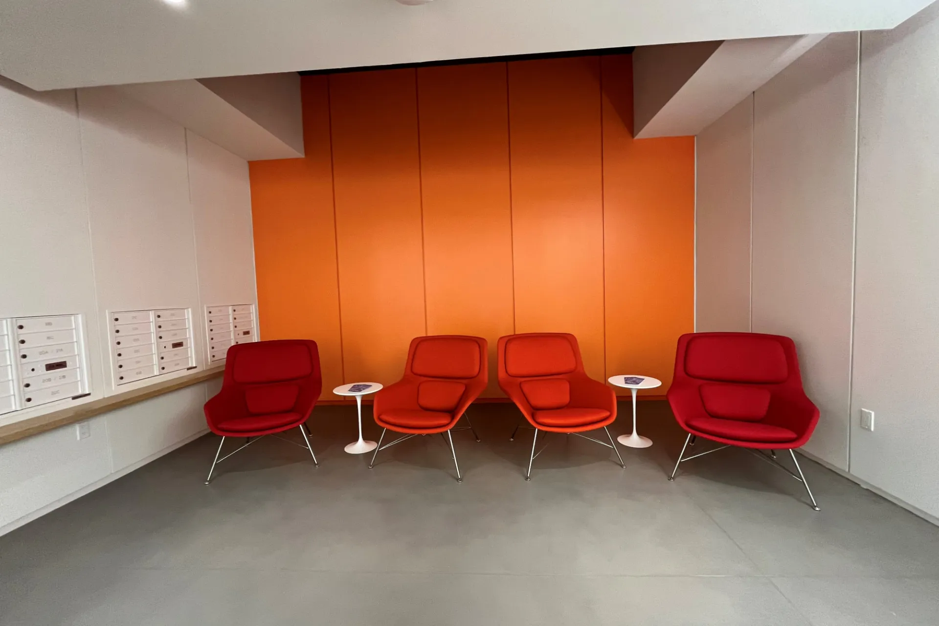 A lobby with an orange accent wall and red lounge chairs.