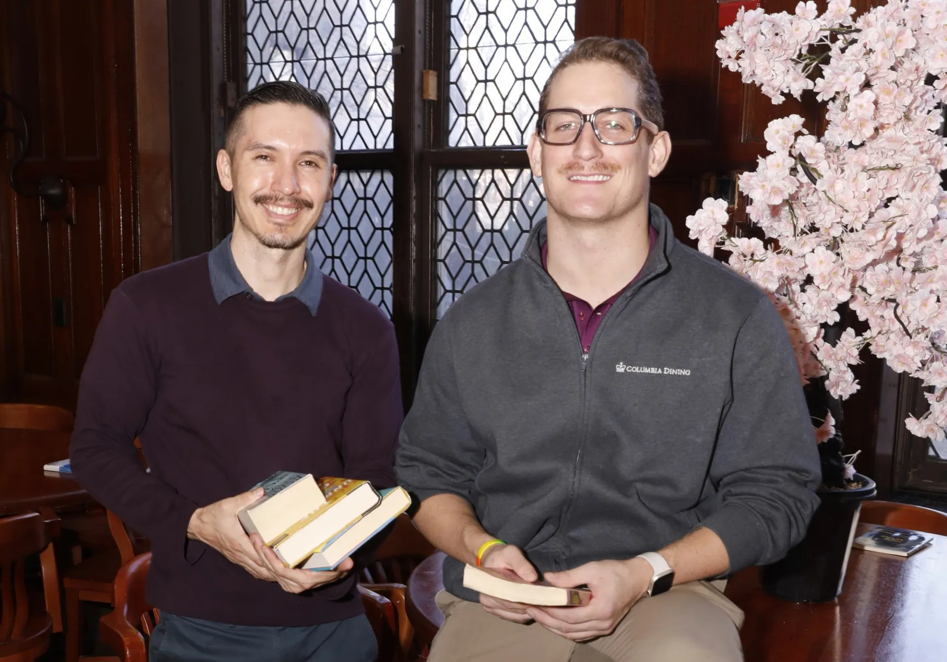 Ben Kimura and Chuck Robinson hold books and smile together in John Jay Dining Hall.