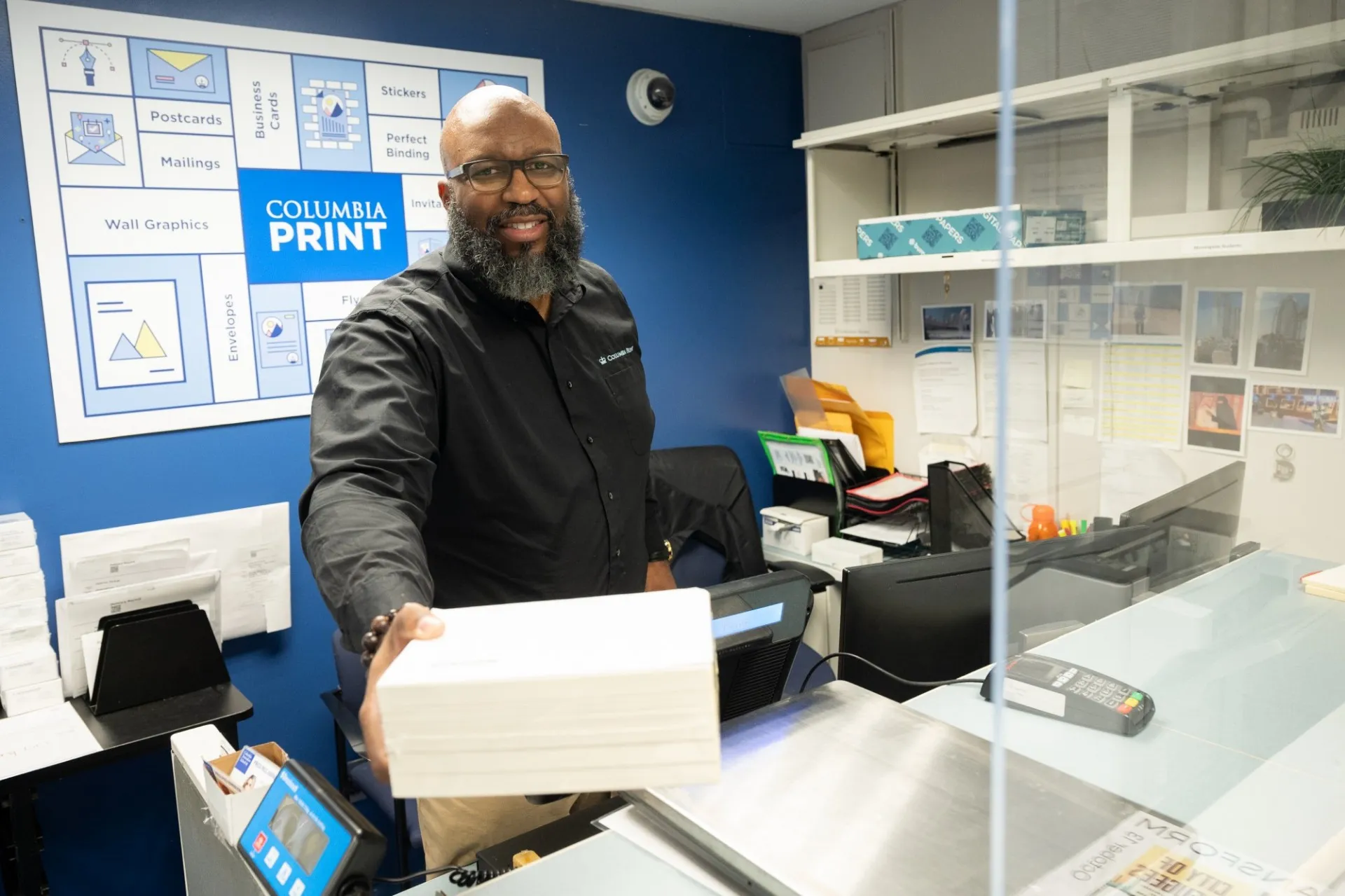 A Columbia Print employee giving out a stack of paper from behind the Columbia Print desk.