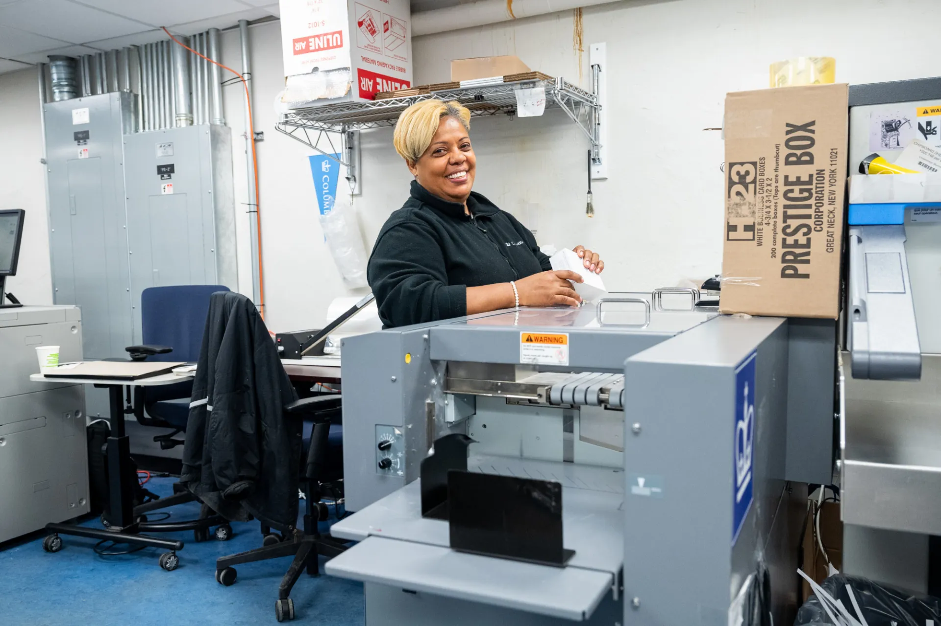 A Columbia Print employee smiles at a machine that is printing out cards.