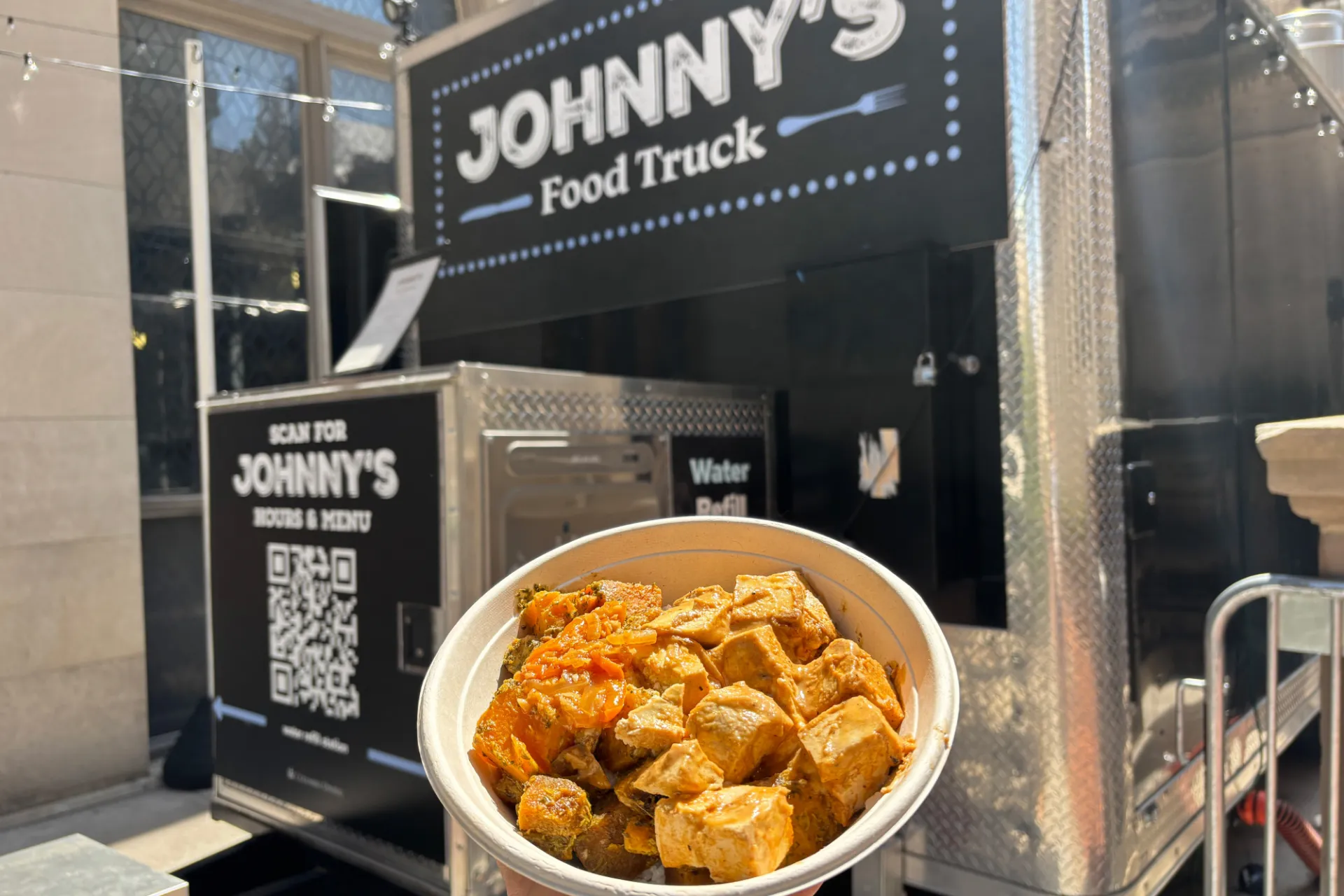 A person holding out a plate of food in front of the Johnny's food truck.
