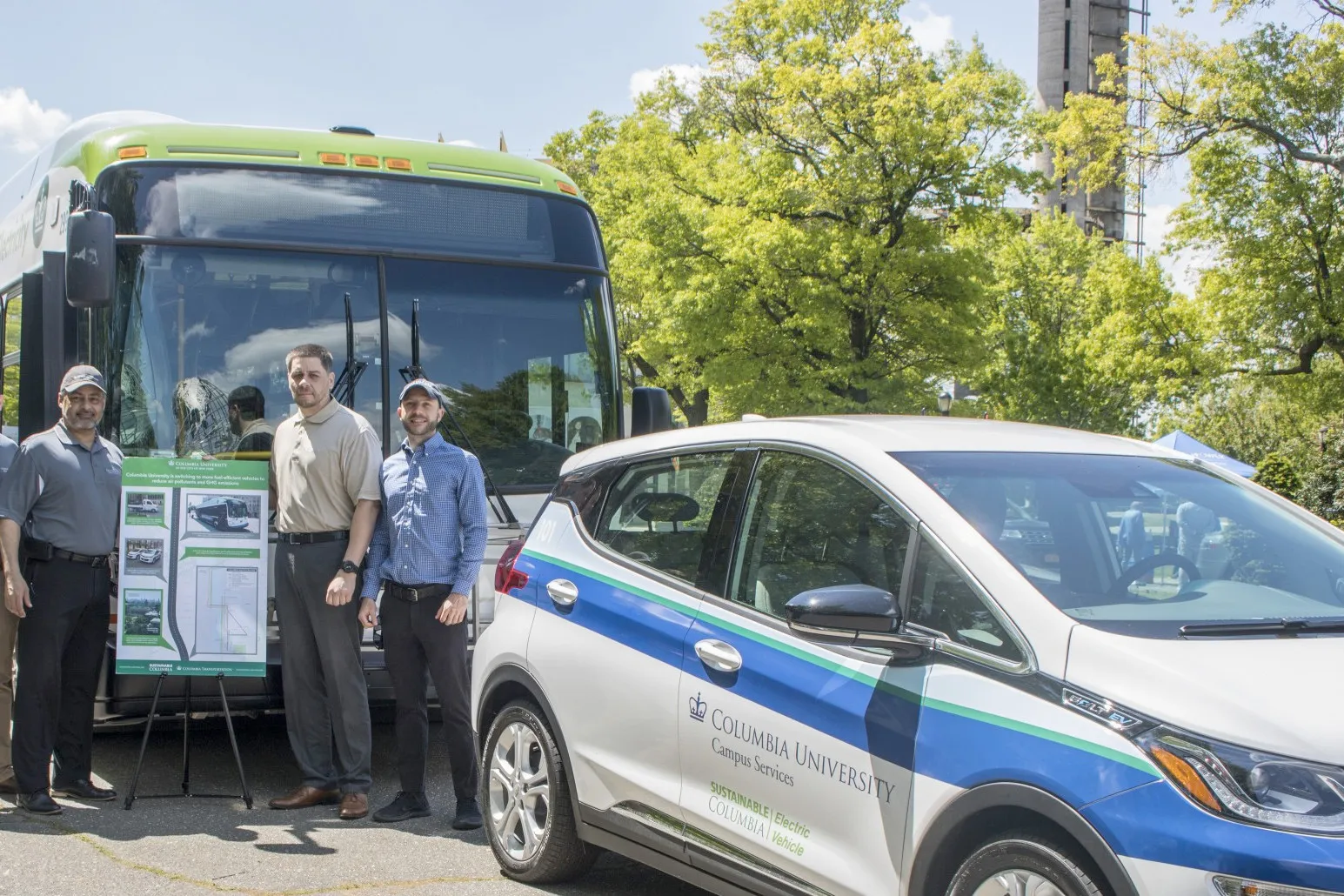 Mike Pagan stands with staff next to Columbia's Intercampus shuttle bus and electric car.