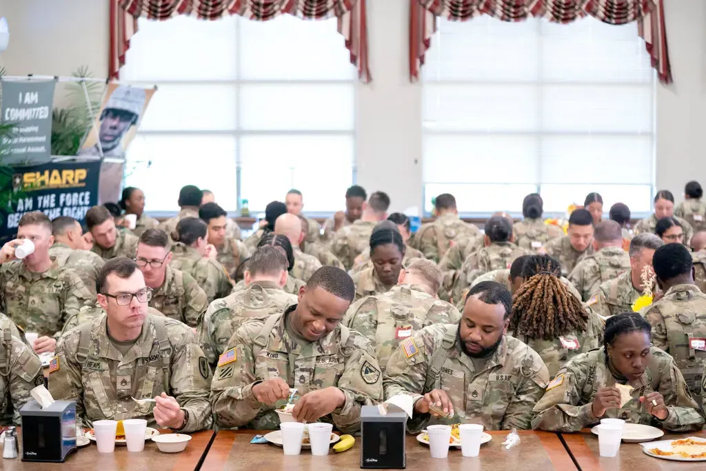 A group of army soldiers eat food in a dining hall.