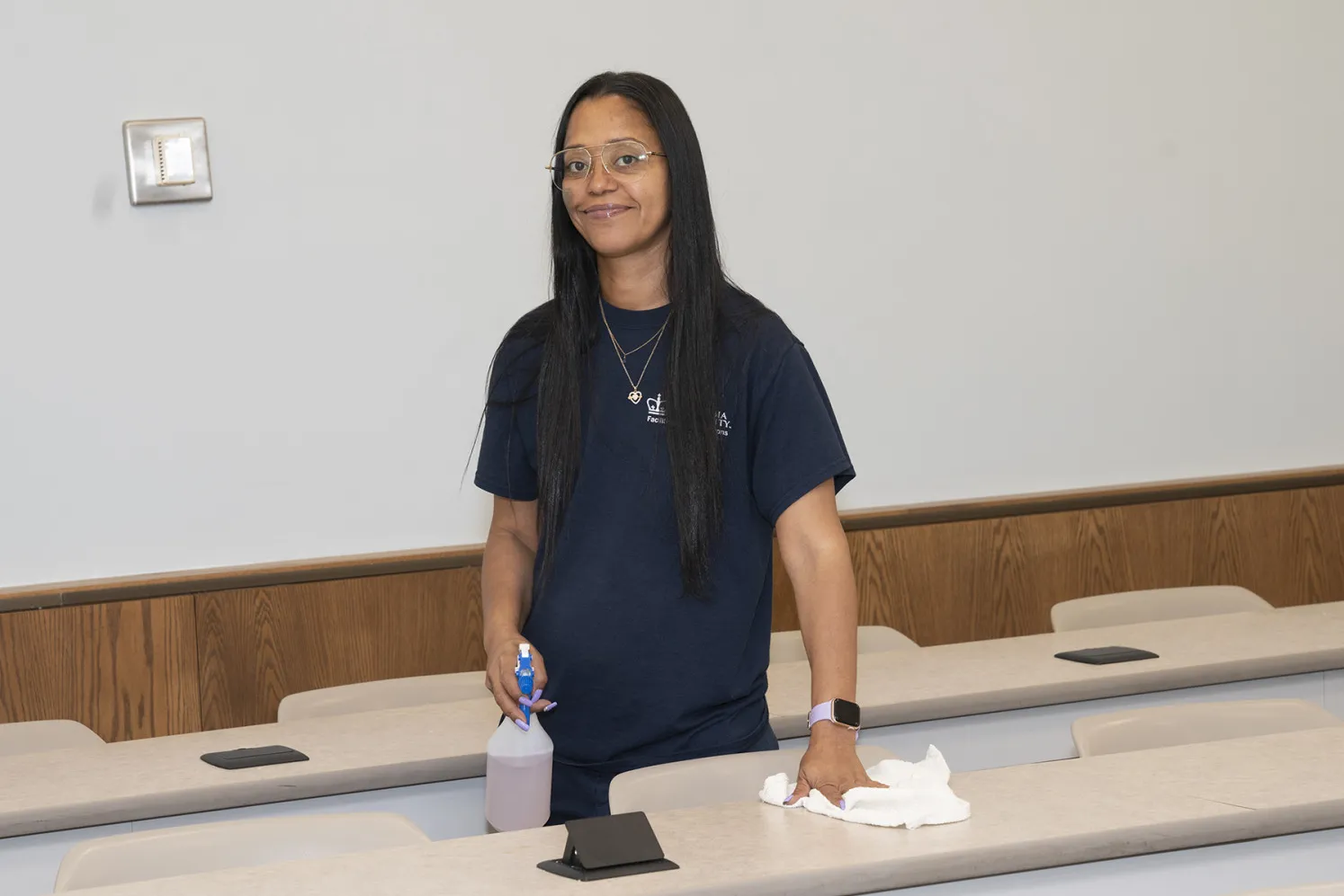 A Facilities and Operations employee wipes down desks in a classroom.