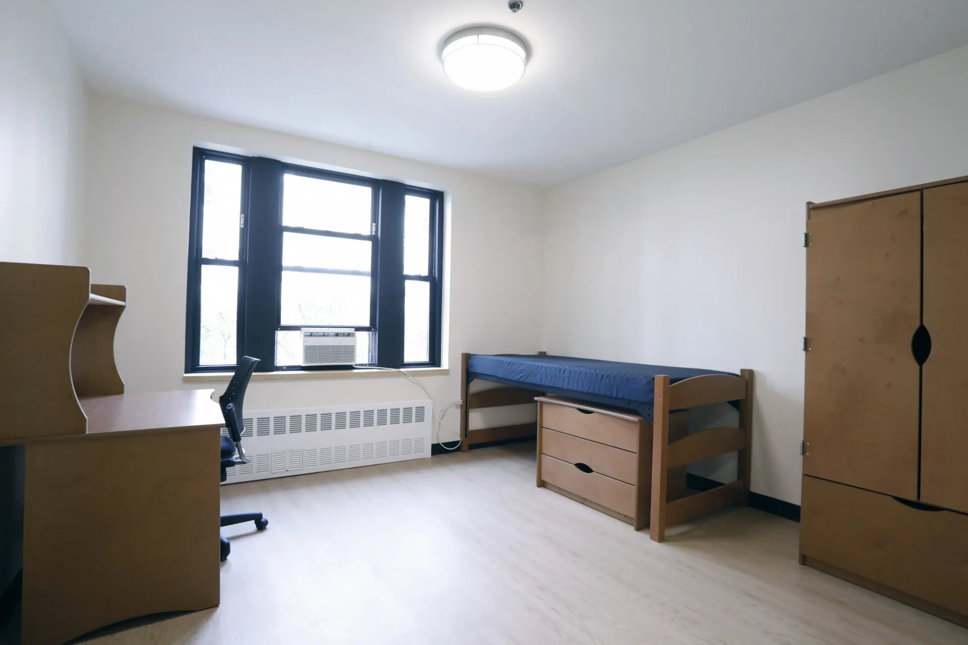 A refreshed dorm room with a bed, desk, and wardrobe closet.