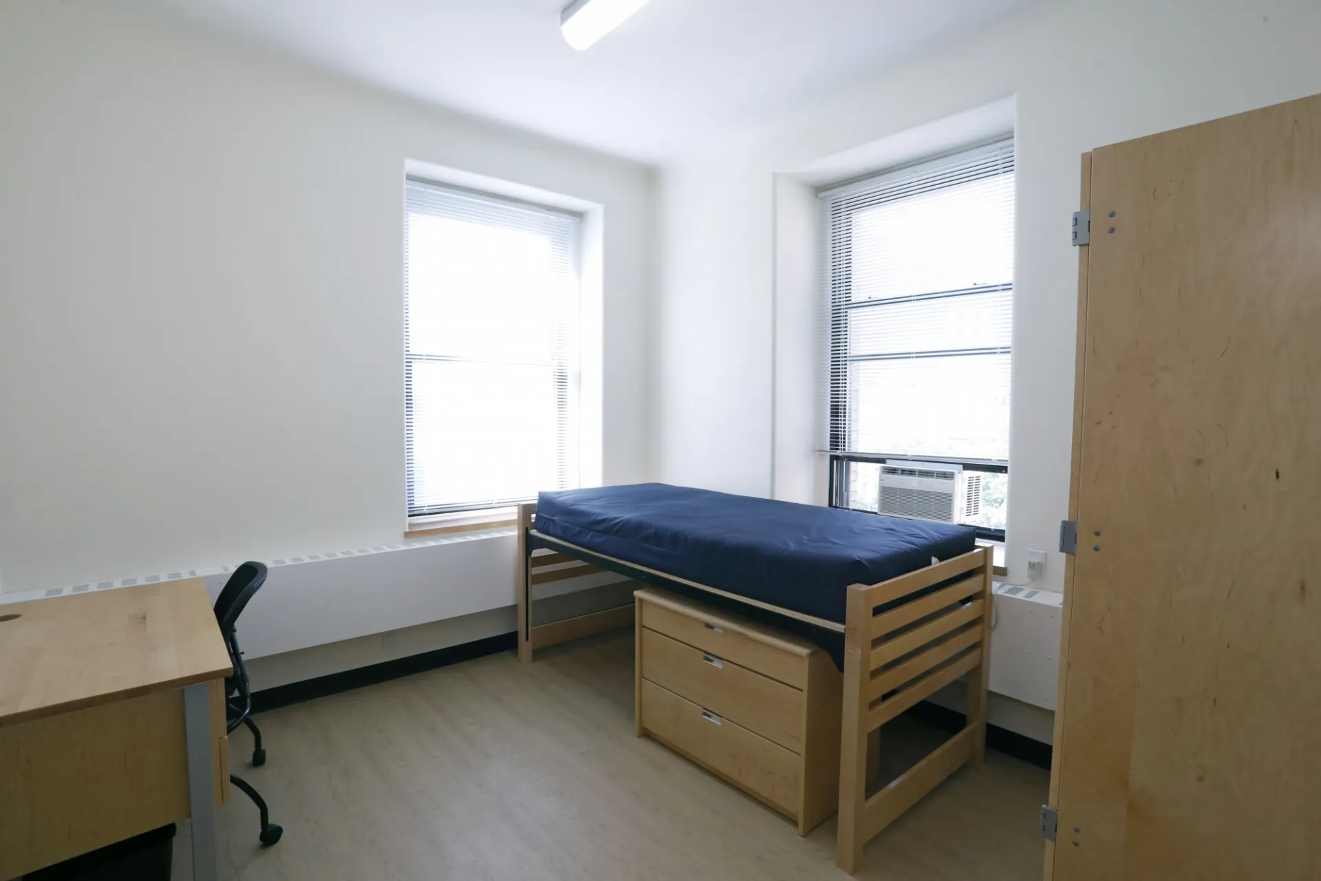 A refreshed dorm room with a bed, desk, and wardrobe closet.